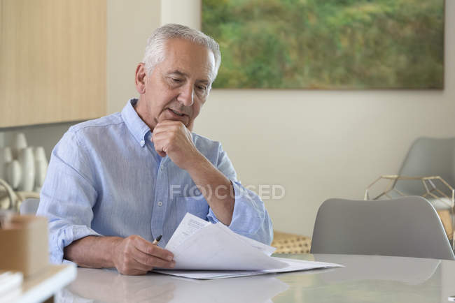 Сосредоточенный старший мужчина делает бумажную работу дома — стоковое фото