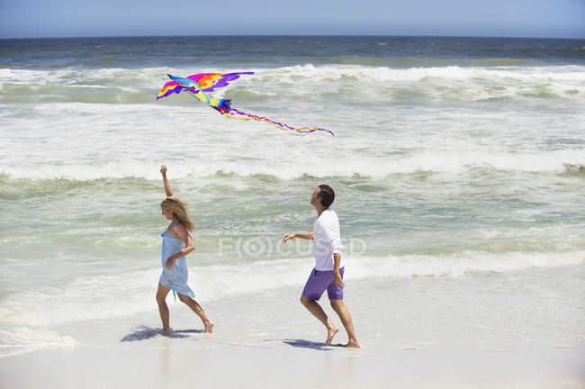 Пара веселится с летающим воздушным змеем на пляже — стоковое фото