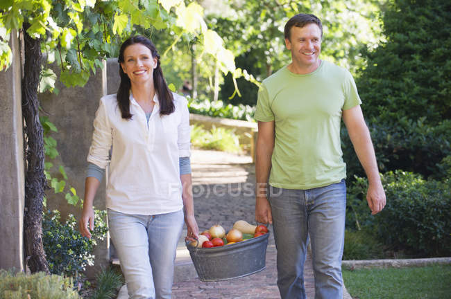 Pareja madura llevando frutas en cesta en el jardín - foto de stock