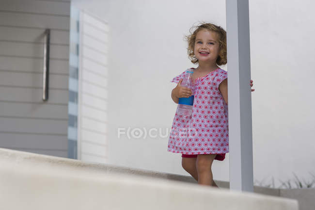 Happy baby girl holding water bottle on porch — Stock Photo