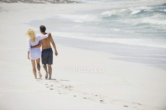 Visão traseira de abraçar casal andando na praia — Fotografia de Stock