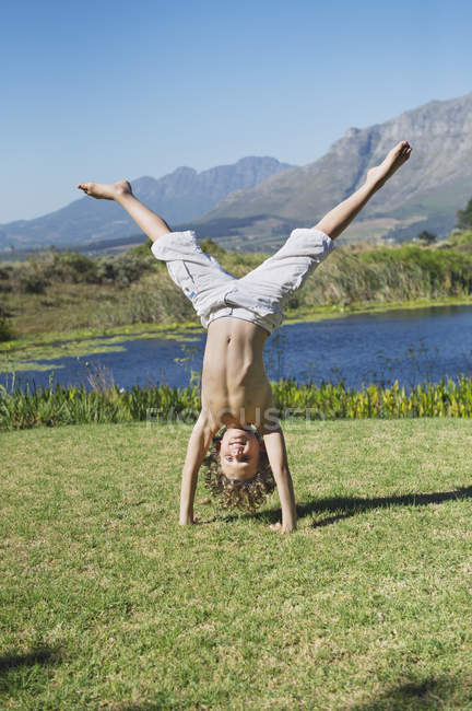 Cute little boy doing cartwheel on grass in nature against mountains — Stock Photo