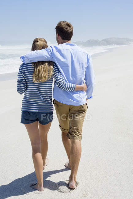 Вид сзади на романтическую пару, гуляющую по пляжу под голубым небом — стоковое фото