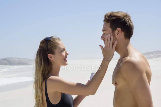 Женщина наносит солнцезащитный крем на лицо мужа на пляже — стоковое фото