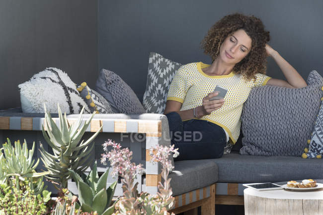 Frau sitzt zu Hause auf Couch und nutzt Smartphone — Stockfoto