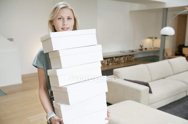 Retrato de mujer rubia llevando cajas de zapatos en la sala de estar - foto de stock
