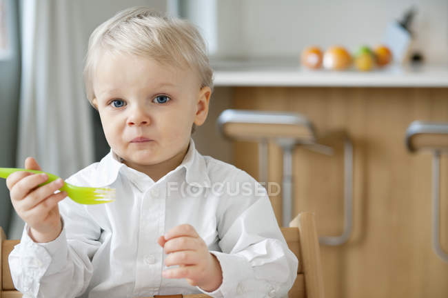 Menino comendo com garfo e fazendo rosto na cozinha — Fotografia de Stock