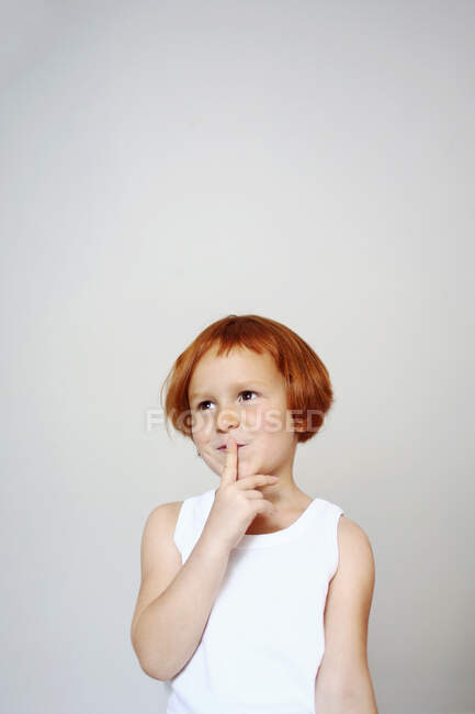 Retrato de uma menina ruiva dentro de casa segurando o dedo na frente da boca com um olhar inquietante em seu rosto — Fotografia de Stock