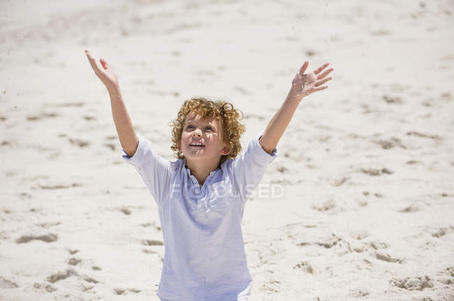 Хлопчик стоїть з руками, піднятими на піщаному пляжі — стокове фото