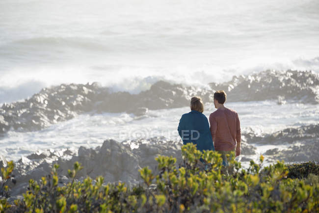 Happy couple looking at wavy sea on beach — Stock Photo
