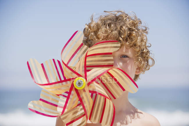 Retrato de menino segurando pinwheel na frente do rosto na praia — Fotografia de Stock