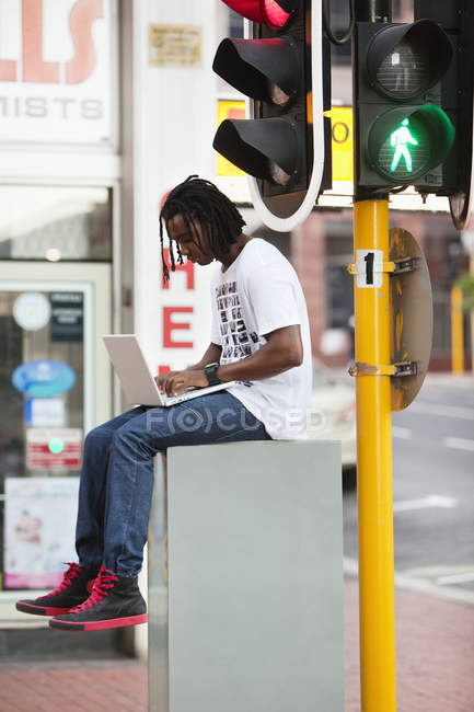 Homem usando laptop perto do semáforo na cidade — Fotografia de Stock