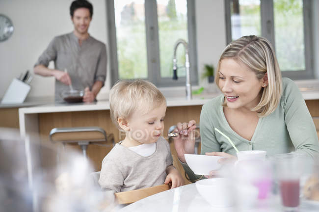 Mujer alimentación desayuno pequeño hijo en cocina - foto de stock