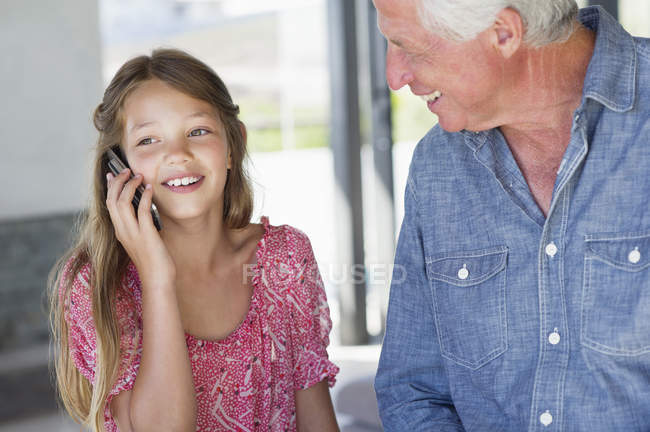 Menina falando no telefone celular com o avô sorrindo em casa — Fotografia de Stock