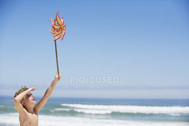 Garçon tenant pinwheel sur la plage sous le ciel bleu — Photo de stock