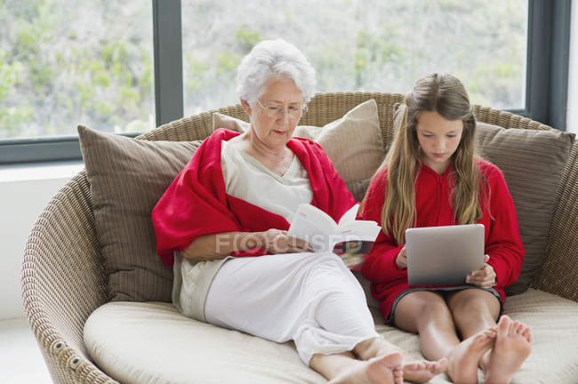Старшая женщина читает книгу с внучкой с помощью цифрового планшета — стоковое фото