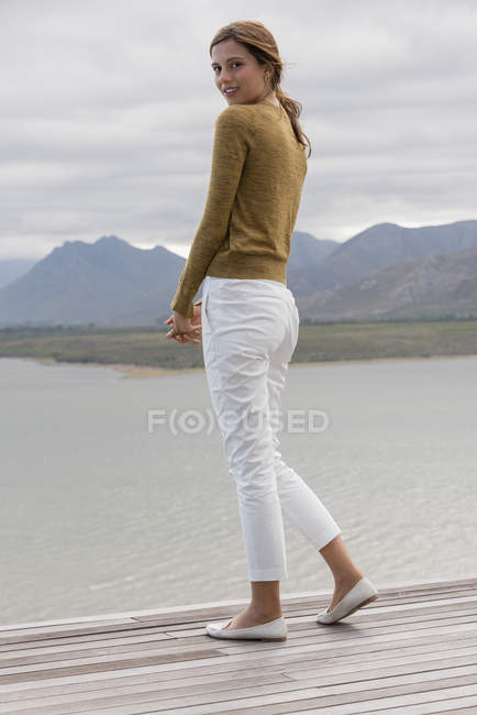 Молодая женщина стоит на палубе у берега озера — стоковое фото