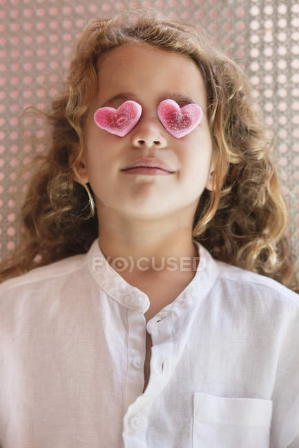 Primer plano de linda niña cubriendo los ojos con juguetes en forma de corazón - foto de stock