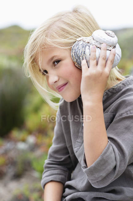 Gros plan de la petite fille qui écoute la coquille de conque dans la nature — Photo de stock