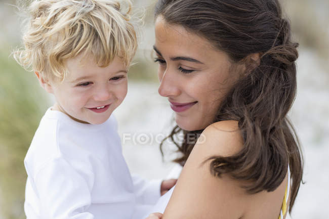 Primer plano de la mujer sonriente sosteniendo al bebé hijo al aire libre - foto de stock