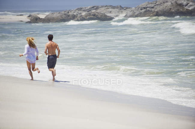 Rear view of couple running on sandy beach — Stock Photo