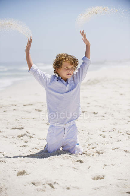 Garçon jouant dans le sable avec les bras levés sur la plage — Photo de stock