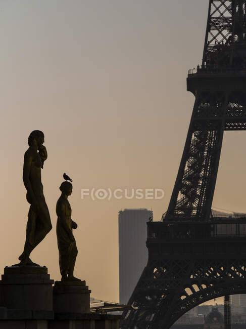 Francia, París, dos estatuas de bronce de colores (1937) en la explanada de Trocad? ro con la Torre Eiffel y la Torre Montparnasse en el crepúsculo - foto de stock