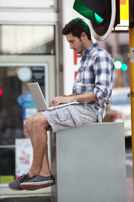 Young casual man using laptop near traffic light in city — Stock Photo
