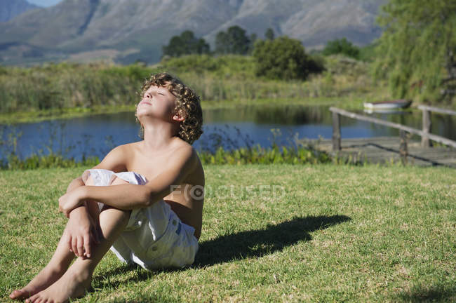 Сорочки маленький хлопчик сидів на очі закриті на траві проти гори — стокове фото