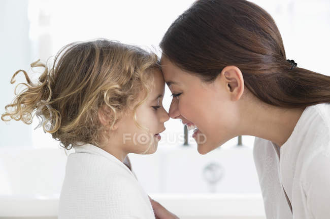 Madre tocando la nariz con una niña envuelta en toalla en el baño - foto de stock