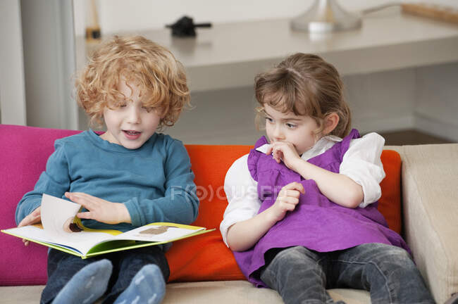 Niño sentado con su hermana y leyendo un libro - foto de stock