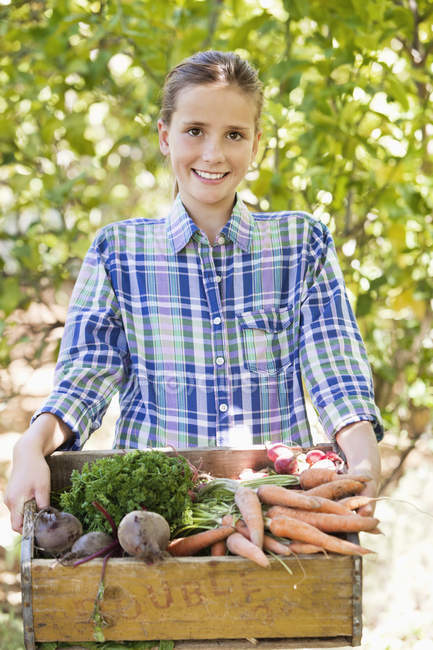 Retrato de menina sorridente segurando caixa de legumes no jardim — Fotografia de Stock