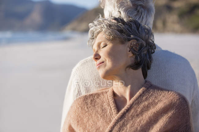 Close-up of relaxed thoughtful senior couple standing back to back on beach — Stock Photo