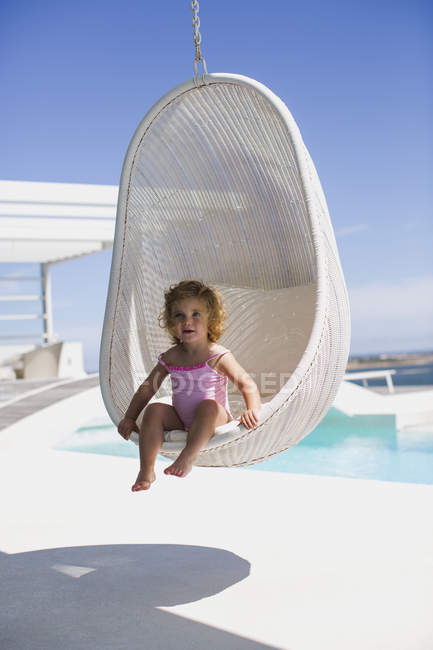 Дитяча дівчинка сидить у плетених гойдалках біля басейну — стокове фото
