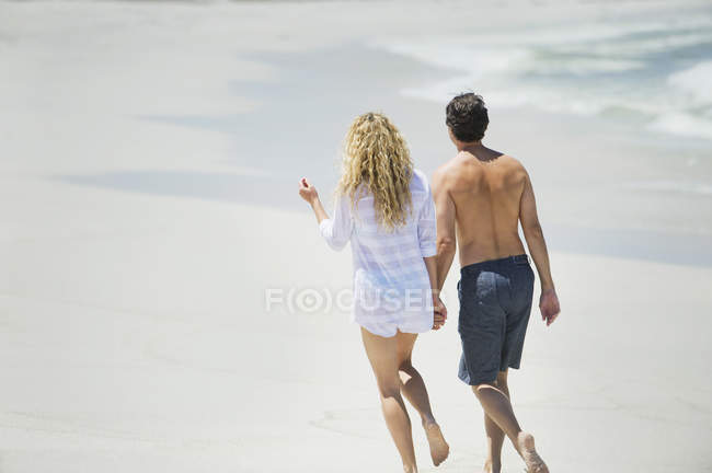 Vue arrière du couple marchant sur la plage tenant la main — Photo de stock