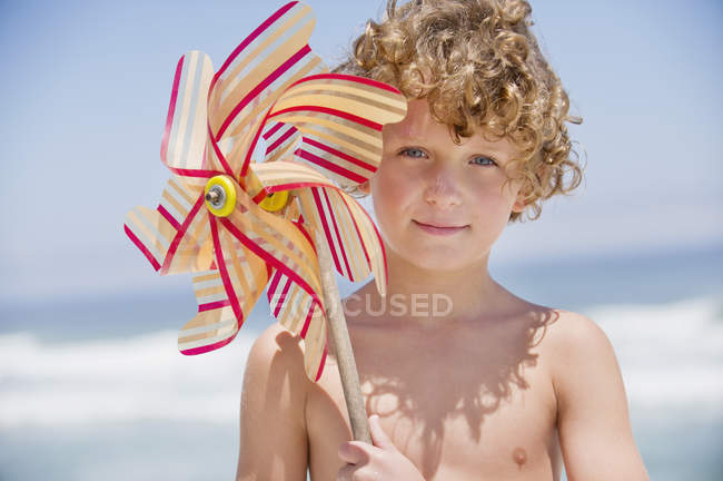 Retrato de niño sosteniendo el molinete delante de la cara en la playa - foto de stock