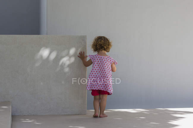 Visão traseira da menina bonito de pé contra a parede — Fotografia de Stock