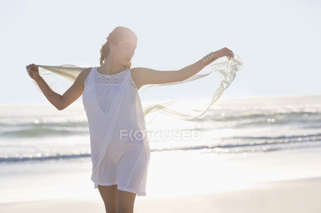 Mujer joven y relajada con los brazos extendidos disfrutando en la playa - foto de stock