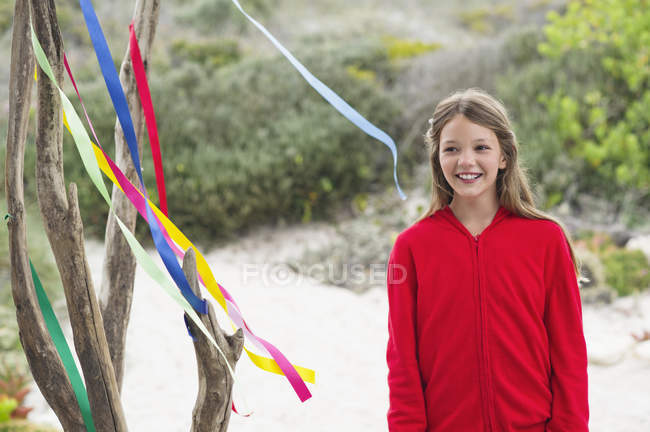 Smiling girl standing near a tree decorated with ribbons — Stock Photo