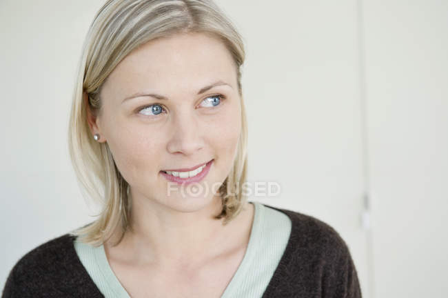 Gros plan d'une femme blonde souriante aux yeux bleus détournant les yeux — Photo de stock