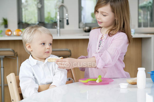 Девочка кормит младшего брата на кухне — стоковое фото