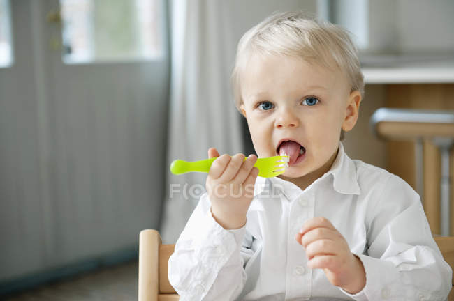 Retrato del chico comiendo con un tenedor en casa - foto de stock