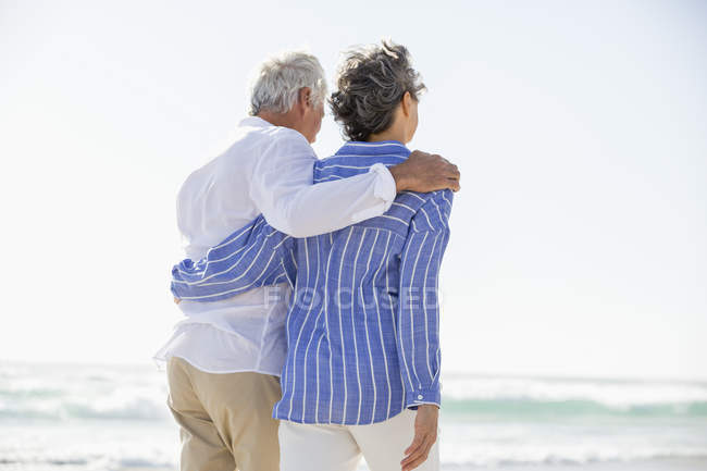 Visão traseira de abraçar casal sênior andando na praia — Fotografia de Stock