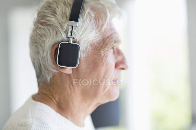 Старший чоловік слухає музику з навушниками і дивиться вбік — стокове фото