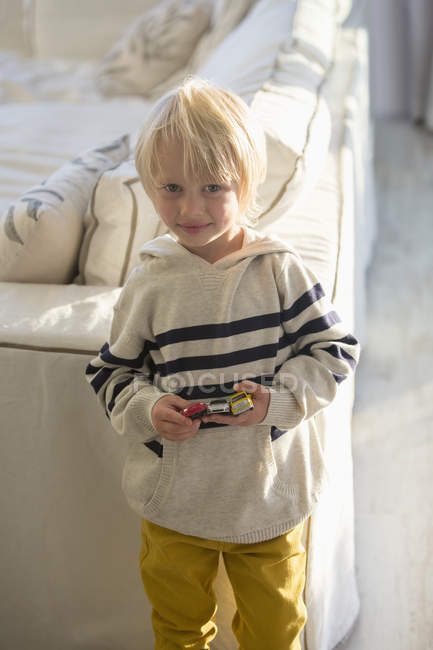 Портрет блондинки маленького хлопчика, який тримає іграшкові автомобілі у вітальні — стокове фото