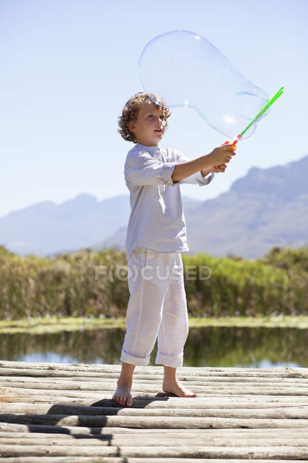 Мальчик играет с палочкой на пирсе в природе — стоковое фото