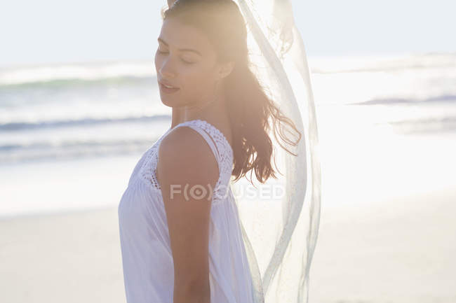 Молода жінка з закритими очима позує на пляжі на задньому світлі — стокове фото