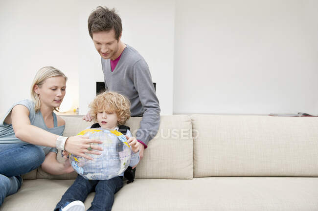 Eltern im Wohnzimmer mit ihrem Sohn, der einen Globus in der Hand hält — Stockfoto
