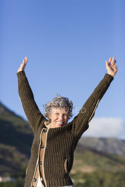 Porträt einer glücklichen Frau, die mit erhobenen Armen in der Natur steht — Stockfoto