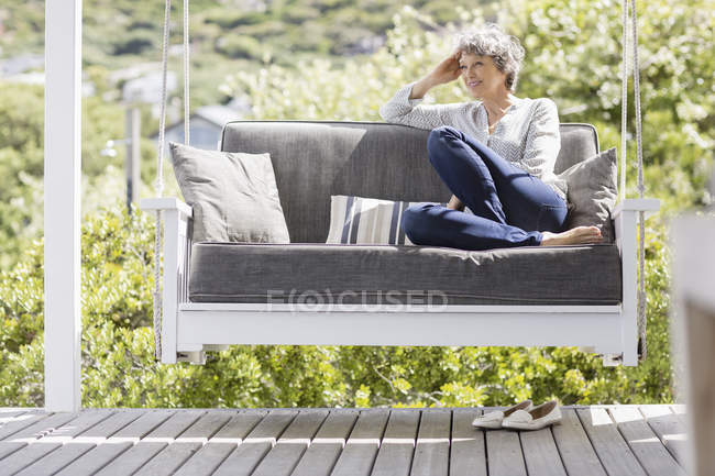 Happy mature woman sitting on swing in porch — Stock Photo
